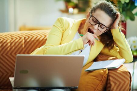 tired working Get X woman in jeans and yellow jacket in the modern house in sunny day study online on a laptop.