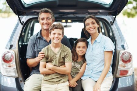 A friendly family sitting together in the open boot of their car